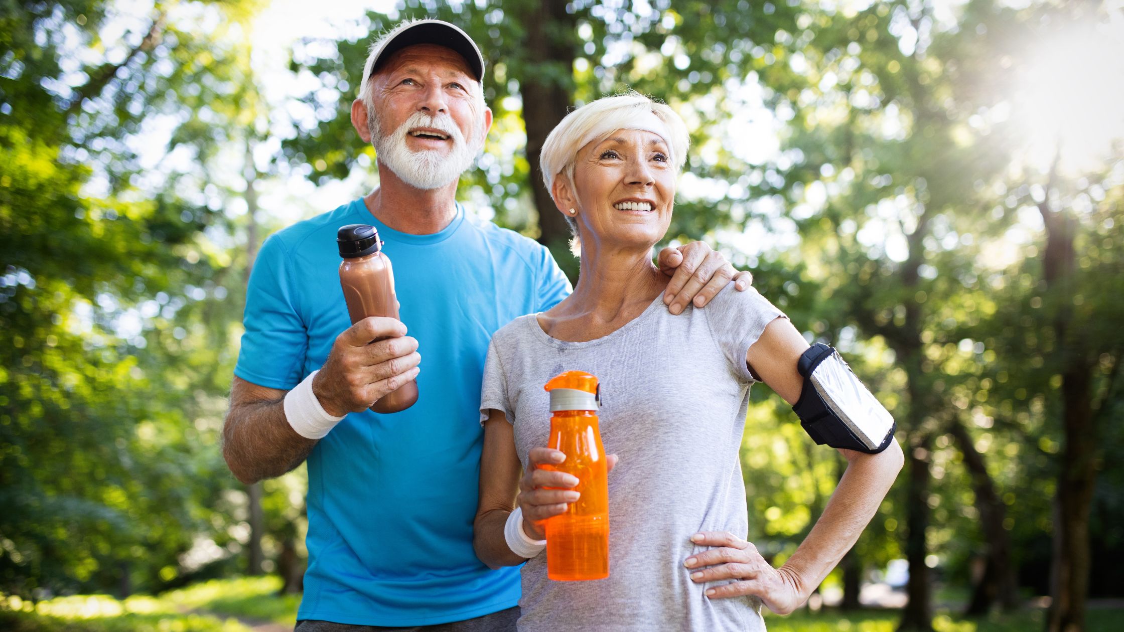 Active older couple enjoying outdoor exercise, holding water bottles, promoting healthy lifestyle and wellness.